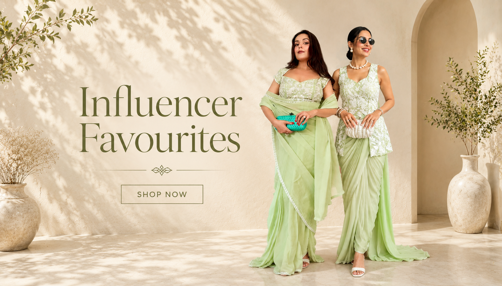 Two women in light green sarees standing in a well-lit room with decorative elements.