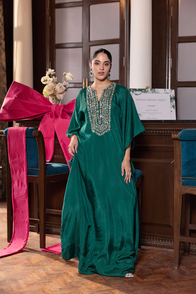 Woman in a green dress with beaded neckline standing in an elegant room with chairs and decorations.